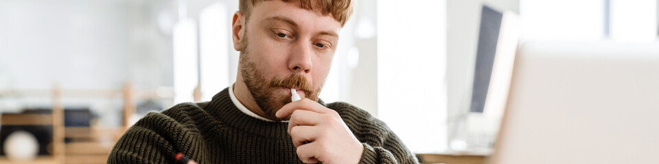Young ginger man working with papers and laptop in office