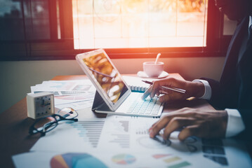 closeup hands of business man working on laptop and using pen making notices in her notebook on wooden table with a cup of coffee. Business concept