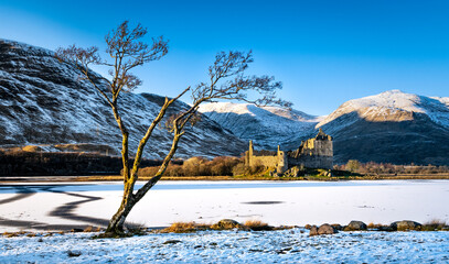 Kilchurn Castle under a blanket of snow - Golden sunset light glistening on the tree and the castle walls - Loch Awe, Argyll, Scotland 