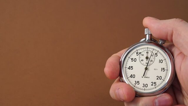 Mechanical Stopwatch in man's hand. Male trainer's hand holding stopwatch on brown background. Retro analog stopwatch in a hand pointing a few seconds isolated on brown background.