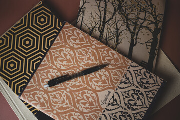 brown notebooks and a notebook with an oriental ornament and a black pen