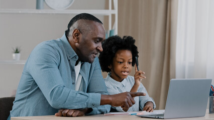 Caring african american father helping little daughter schoolgirl do homework adult parent or tutor explaining to child computer educational processes on laptop e-learning distance learning at home