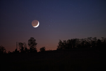 Tree silhouettes, stars, planets and Moon on evening sky.