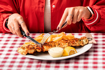 A girl using a knife and fork to eat traditional Greek grilled meat - souvlaki