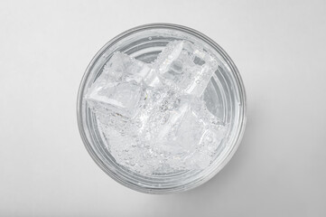 Glass of soda water with ice on light background, top view