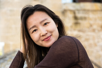 Portrait of a 29 year old Asian American woman, leaning on old stones, hands in the hair