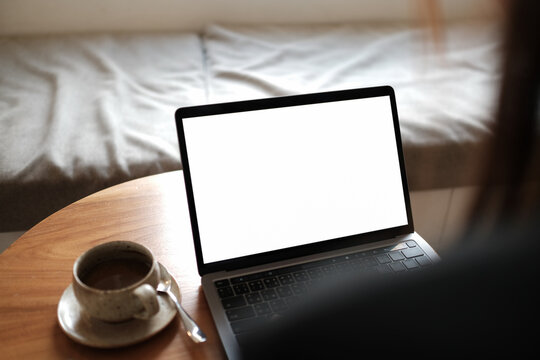 Mockup image of a businesswoman using laptop with blank white desktop screen with coffee cup on wooden table in cafe.