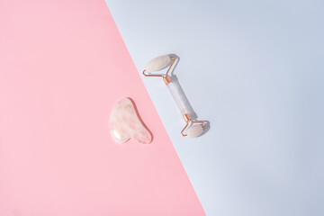 Pink Gua Sha facial massage tools on a double background. Jade roller made of rose quartz on a blue and pink background. tightening and toning procedure at home.