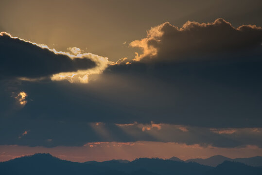 Sunlight rays from cloud hole over mountain range silhouette in an evening © Chartchai