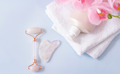 Obraz na płótnie Canvas Quartz jade roller, Gua Sha massager and a bottle of oil with a towel on a blue background. Massage tool for facial skin care, the concept of SPA treatments