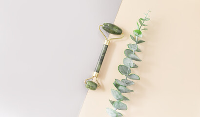 Fototapeta A green jade roller and a gua sha stone for facial massage and a branch of eucalyptus on a double background. Accessories for home beauty and self-care. A roller for the face. Top view, flat position. obraz