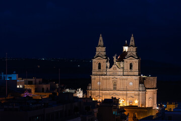 Fototapeta na wymiar Mellieha, Malta - 01 07 2022: The cathedral twin towers and the valley by night, high angle view
