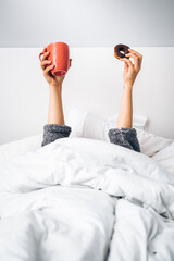 Woman's hands holding a cup of coffee and a homemade donut in the morning upon waking up