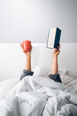 Woman's hands holding a cup of coffee and a book in the morning upon waking up