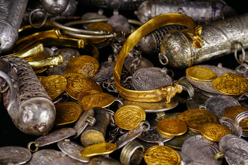 A lot of stacked gold bullion bars and gold coins and silver coins in a treasure sack. Treasure background. 
gold and silver jewelry. Ancient treasure. Pirate treasure and gold and silver filled crate
