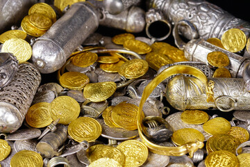 A lot of stacked gold bullion bars and gold coins and silver coins in a treasure sack. Treasure background. 
gold and silver jewelry. Ancient treasure. Pirate treasure and gold and silver filled crate
