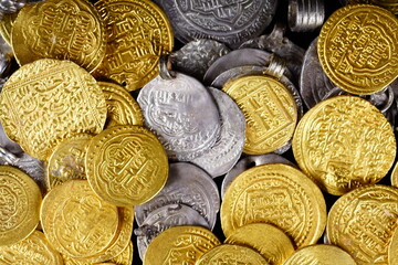 A lot of stacked gold bullion bars and gold coins and silver coins in a treasure sack. Treasure background