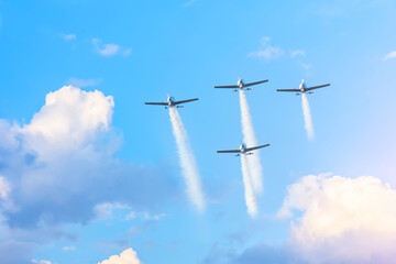 Four planes flying in formation leaving a white smoky trail among the clouds.