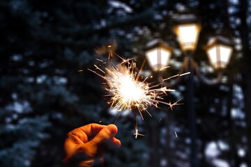 Hand holding sparkler firework firing with sky in background, concept of new year