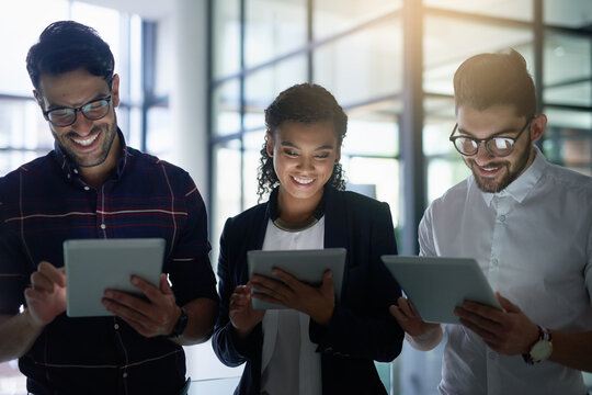 Syncing their devices and success. Shot of three colleagues using digital tablets while standing together in an office.
