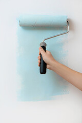 Woman hand painting white wall with blue dye.