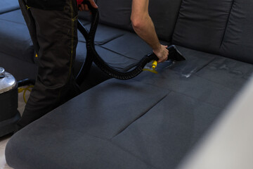 Man dry cleaner's employee cleaning sofa with professionally extraction method