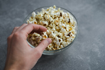 hand takes popcorn from a bowl on the table top view