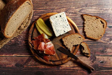 Snack with Italian farm ham, Gorgonzola blue cheese and farmhouse bread served on a round wooden board. Top-down view.