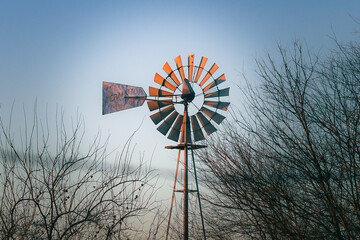 Windmill on a farm with tree branches against a blue sky