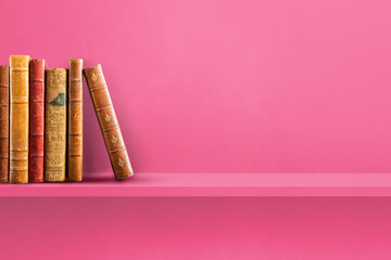Row of old books on pink shelf. Horizontal background