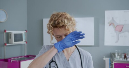 Young beautiful veterinarian standing in office and feeling tired after checkup. Woman standing in veterinary hospital and taking off her glasses. Concept of pets care, veterinary, healthy animals