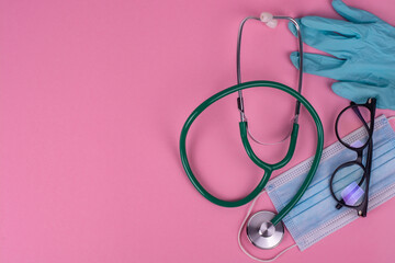 Doctor's stethoscope, mask and gloves on a pink background.