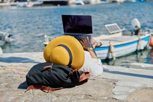 Woman in hat typing on laptop, water bay boat background