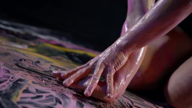 modern artist woman is drawing by her body, lying on floor and smearing paints in workshop