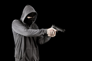 Robber wearing hoodie and balaclava holding pistol. Isolated on black background. Crime concept.