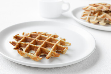 Waffles on white plates close-up and a cup of milk on a white table, tasty breakfast concept