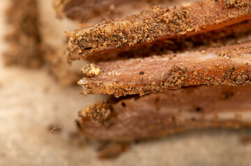 A piece of homemade bacon with pepper on white oiled paper, close-up, selective focus.