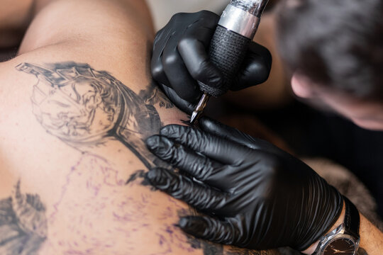 Male tattoo artist with black sterile gloves and a tattoo machine fills a tattoo, close-up