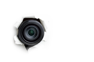 Concept of paparazzi or hidden camera, camera lens looks out through a hole in white paper wall