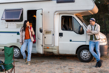 Glad loving couple is standing near the micro bus and looking at each other in the forest. Woman is...