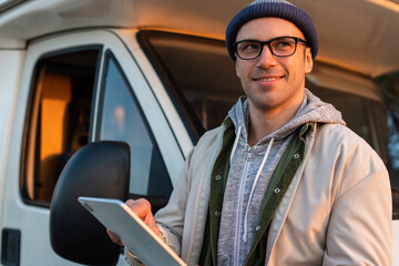 Waist up portrait view of the caucasian man holding tablet and browsing internet while standing at the forest near his car