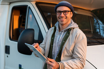 Cheerful caucasian man standing near the motor house and looking something at the tablet while...