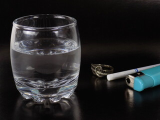 A shot of vodka on a dark background. In the background a lighter, a cigarette, a ring