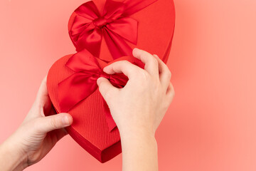 Red box in shape of heart. Gift box for Valentine's Day in the kids hands. Isolated on pink background.