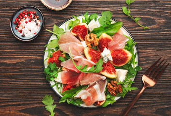 Summer fig salad with jamon, blue cheese, walnuts, arugula on old wooden kitchen table background, top view, copy space