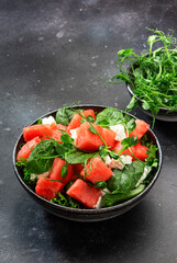 Fototapeta na wymiar Summer watermelon salad bowl with goat cheese, spinach and pea sprouts on gray table background, top view, copy space