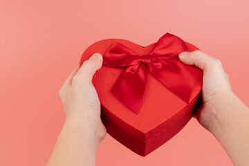 Red box in shape of heart. Gift box for Valentine's Day in the kids hands. Isolated on pink background.