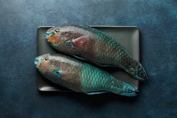 Raamstickers Fresh raw parrot fish cooking on blue stone background © kobeza