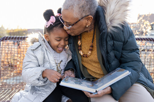 Affectionate grandmother reading story to granddaughter on bench