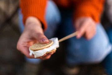 Close up photo of roasting marshmallows over the fire near in camping. Focus on female hands with...